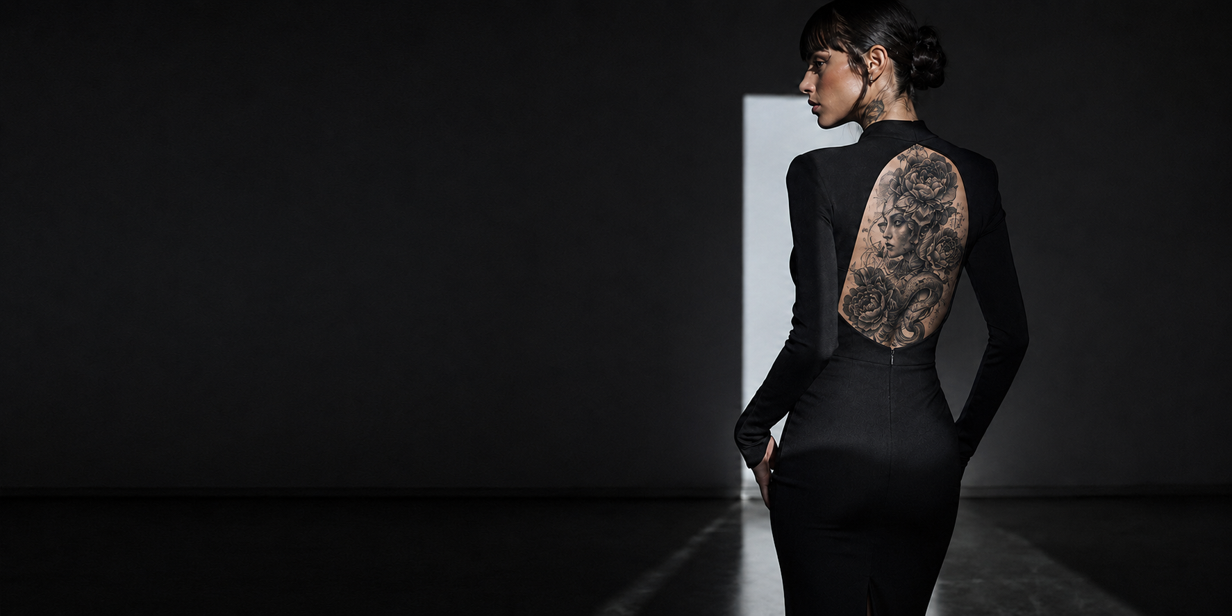 Silhouette vêtue de noir dont l’ouverture au dos encadre un tatouage artistique